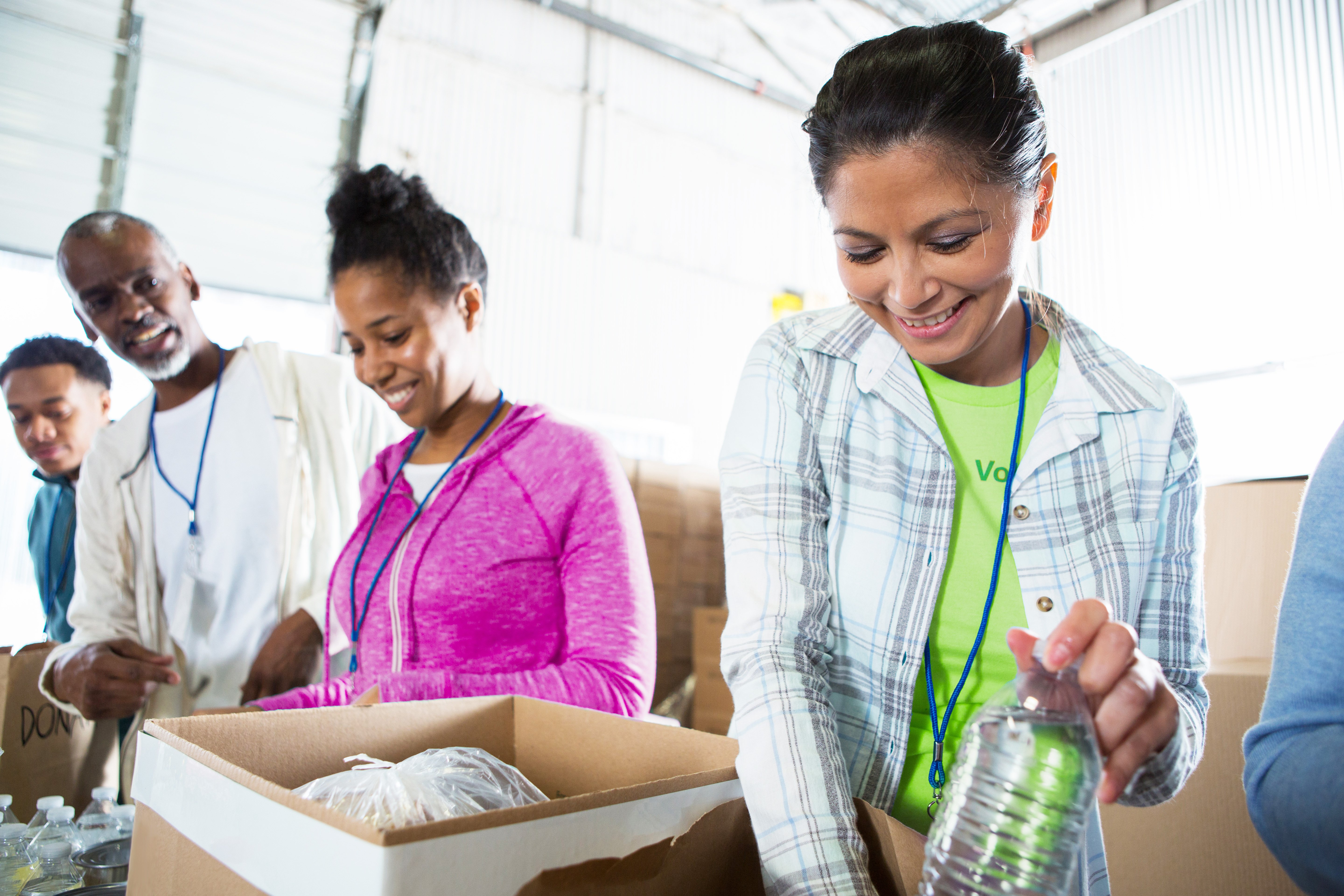 Cheerful group of friends volunteer together in a local food bank. They are packing or unpacking donated food and water.