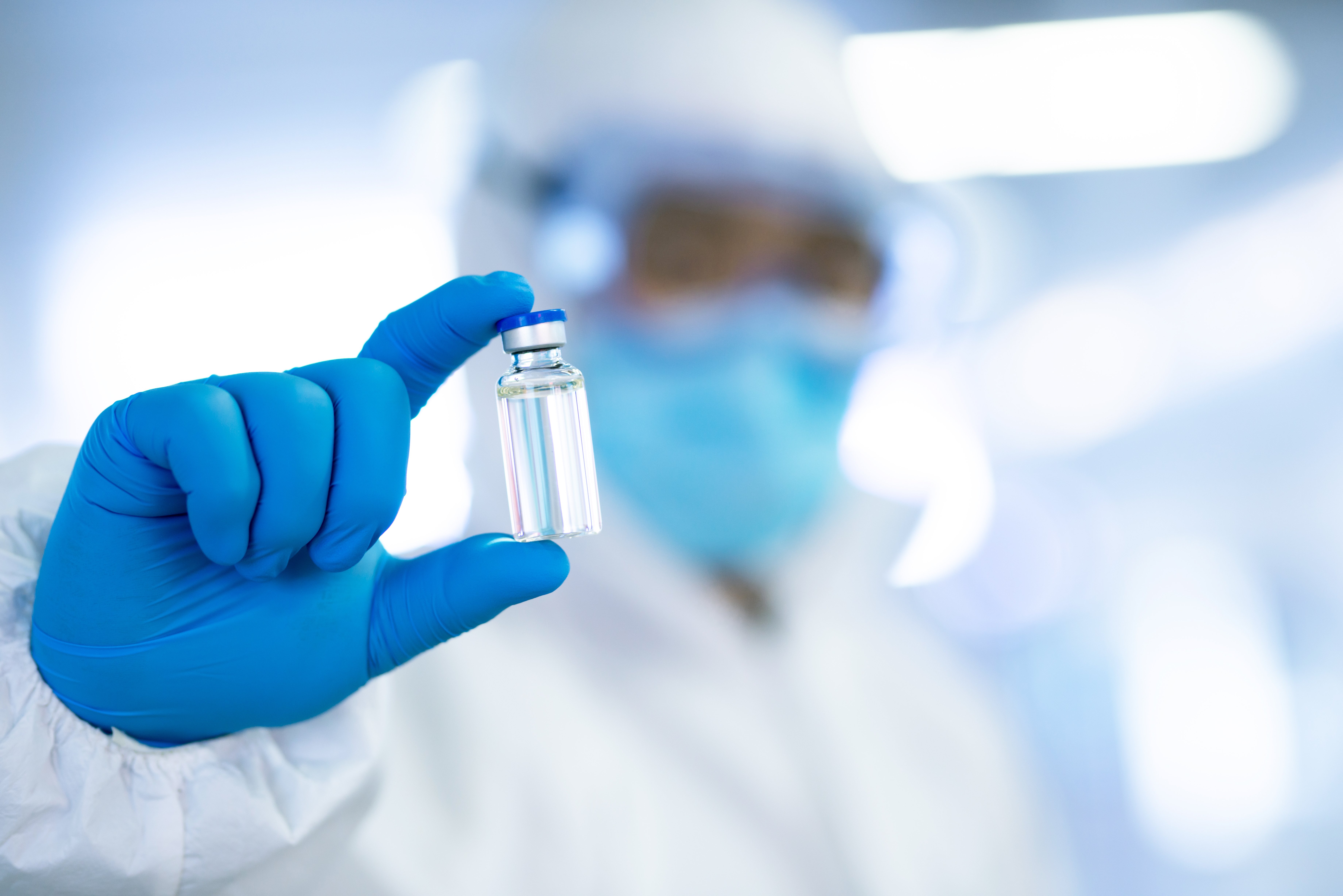 Doctor wearing latex gloves and goggles holds vaccine vial