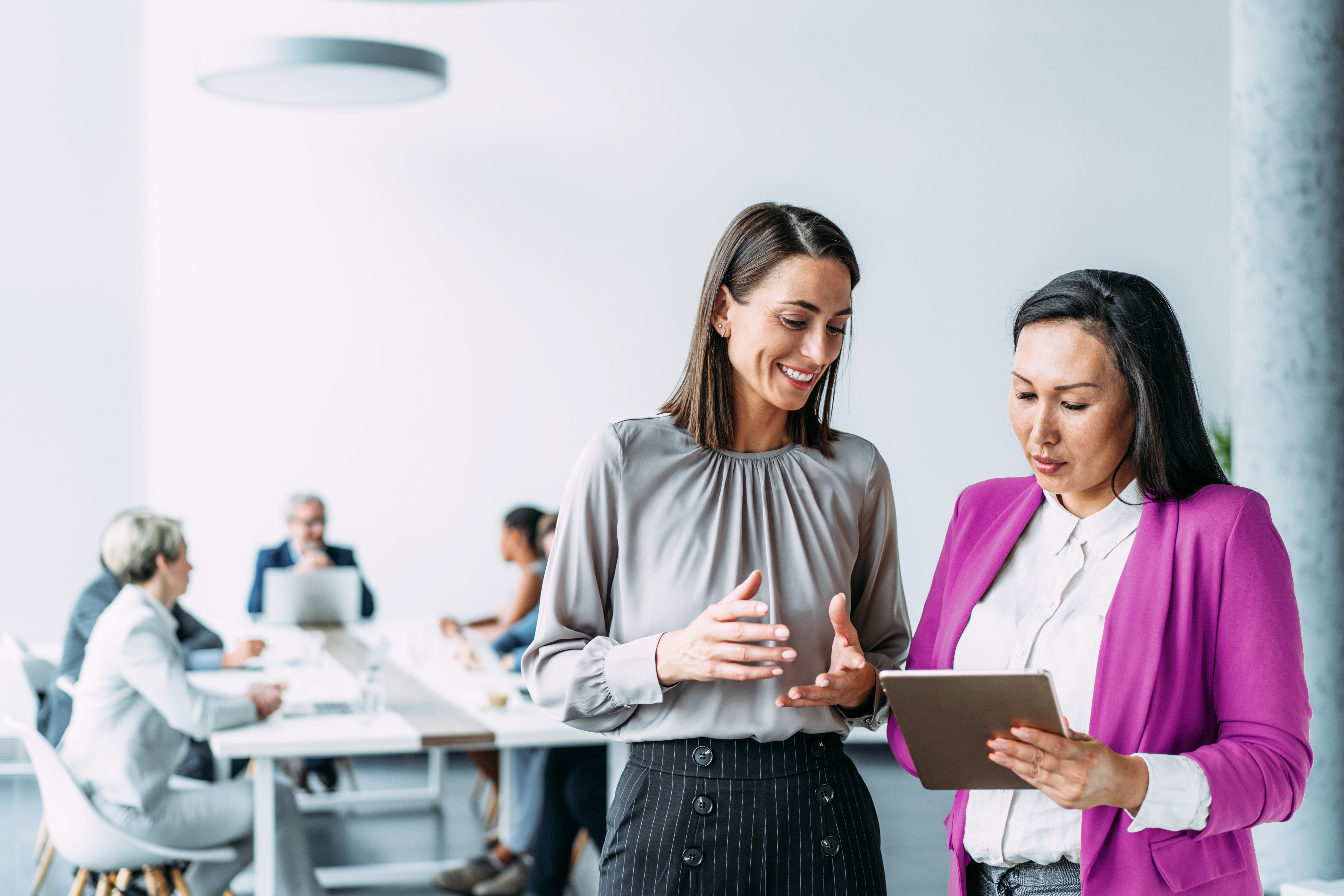 Businesswomen in meeting using digital tablet and discussing business strategy.