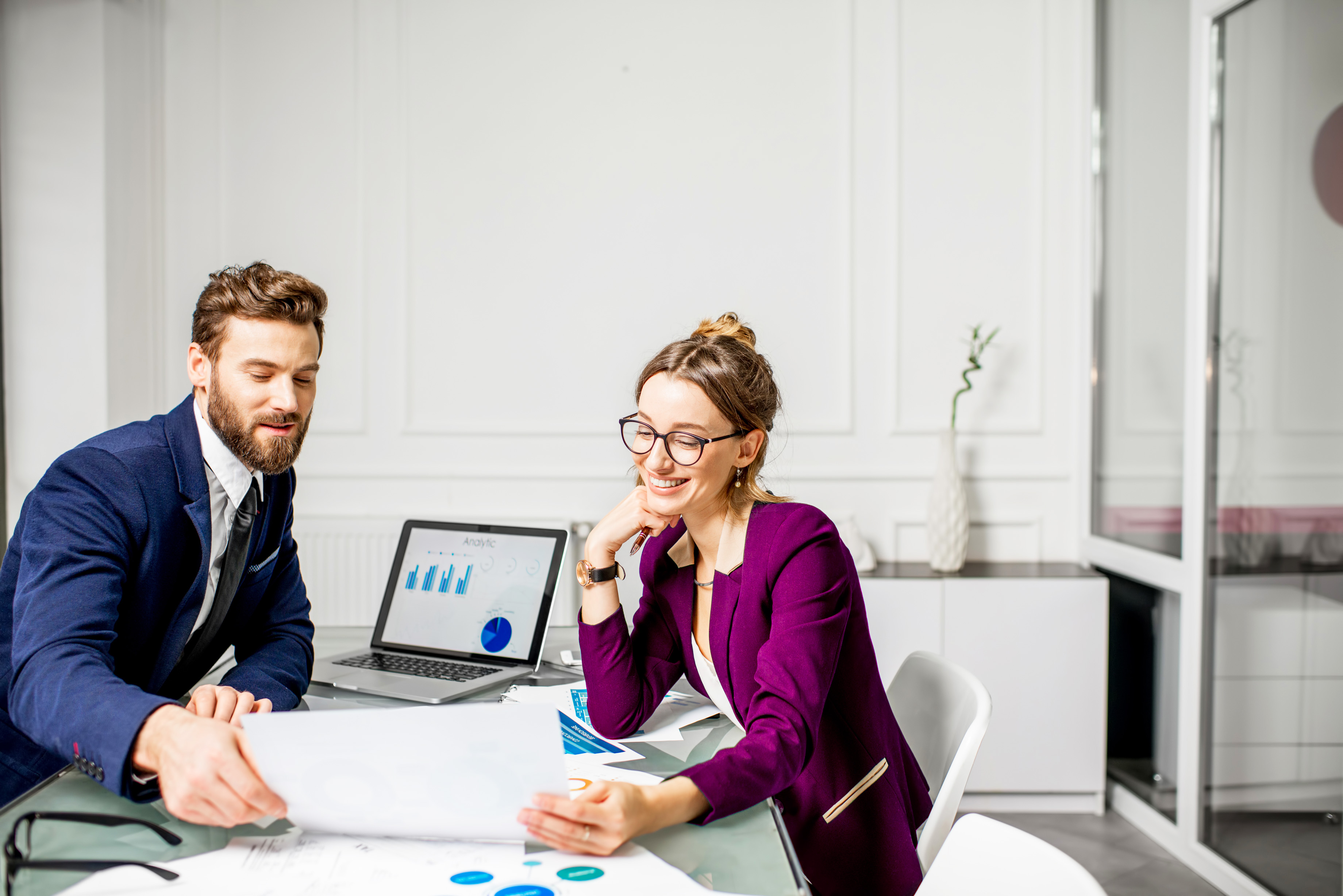 Marketer or analytic manager team dressed in suits working with paper charts and laptops at the white office interior